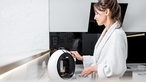 Innovación en electrodomésticos - Mujer en una cocina doméstica utilizando una cafetera para preparar un café expreso.